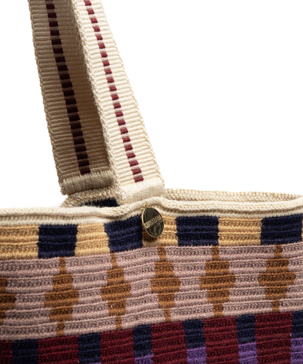 Close-up of the woven shoulder strap attachment and ribbed crochet upper edge with a small metal charm