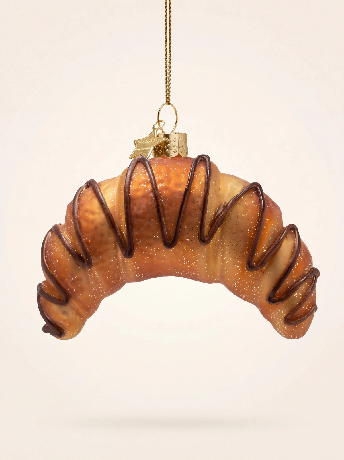 Glass croissant Christmas ornament with painted chocolate drizzle and fine glitter hanging from a gold cord