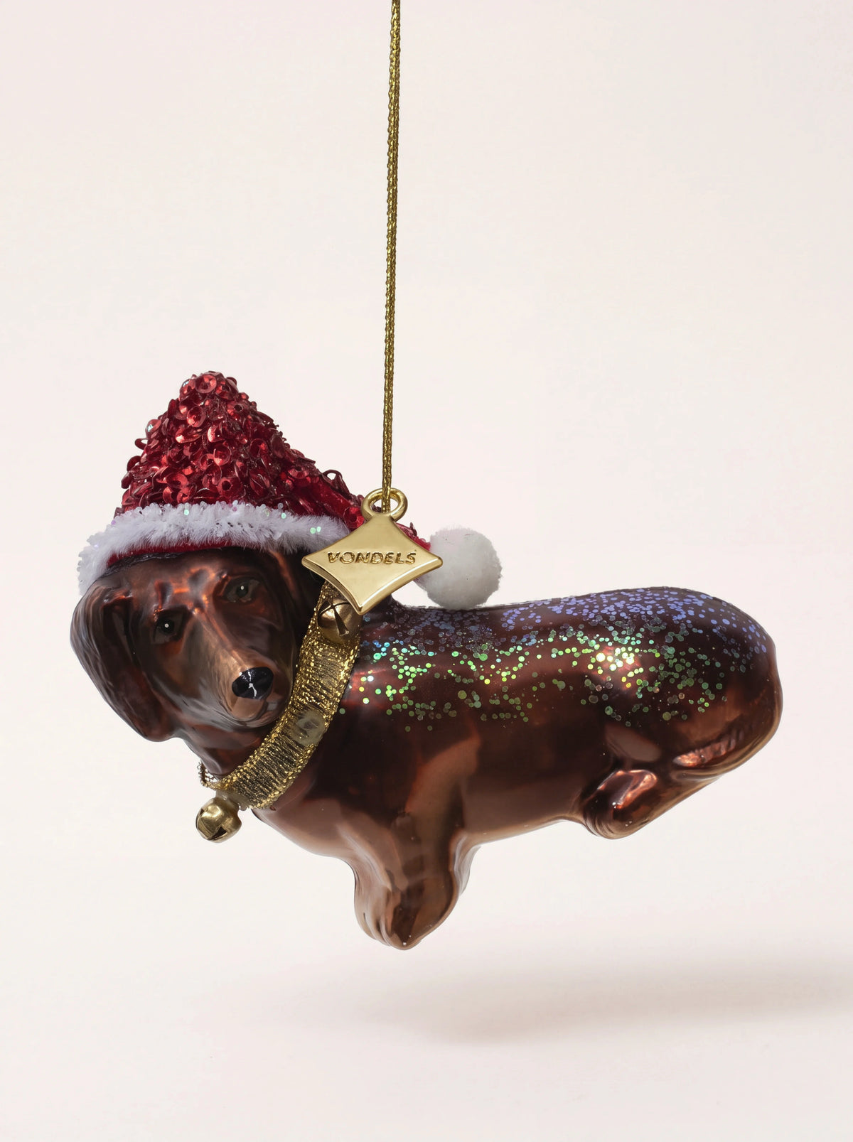Dachshund glass ornament with a red sequined hat, gold bell collar and glitter across its back