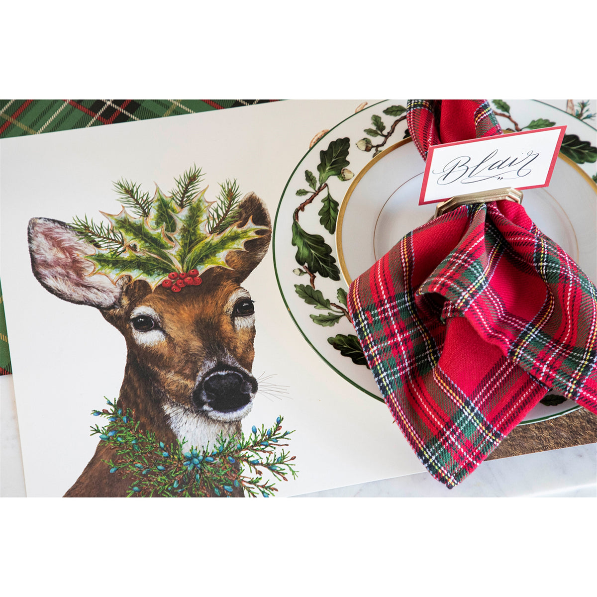 Paper placemat on a set table beside a plate with a red tartan napkin and place card reading "Blair