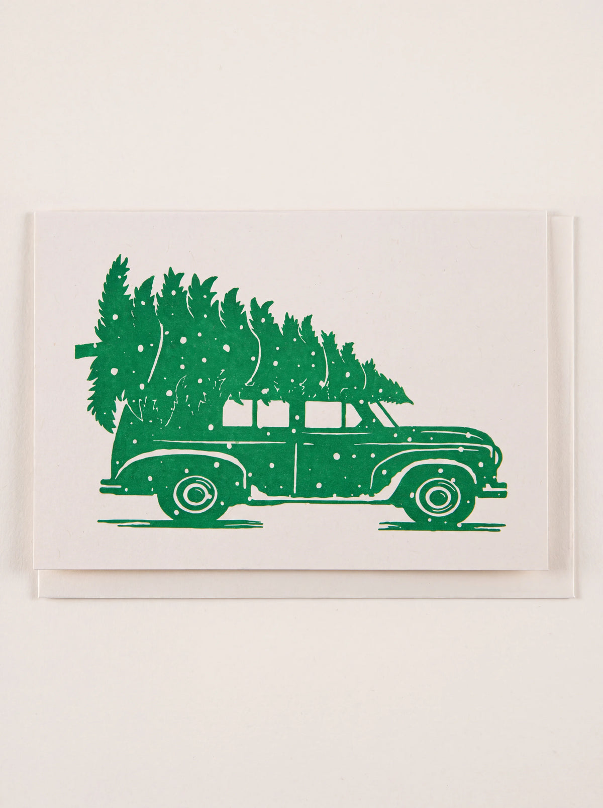 Letterpress Christmas card printed with a green vintage car carrying a tree, shown on a white envelope