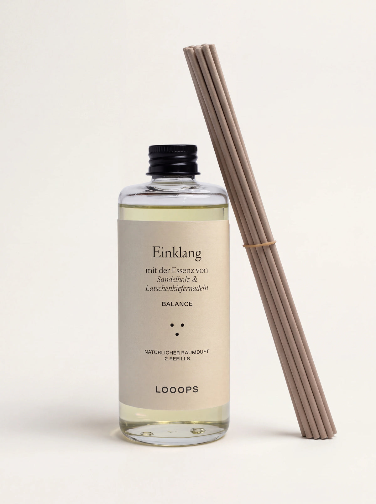 Reed diffuser refill in a clear glass bottle with a black screw cap, shown beside a bundle of reed sticks