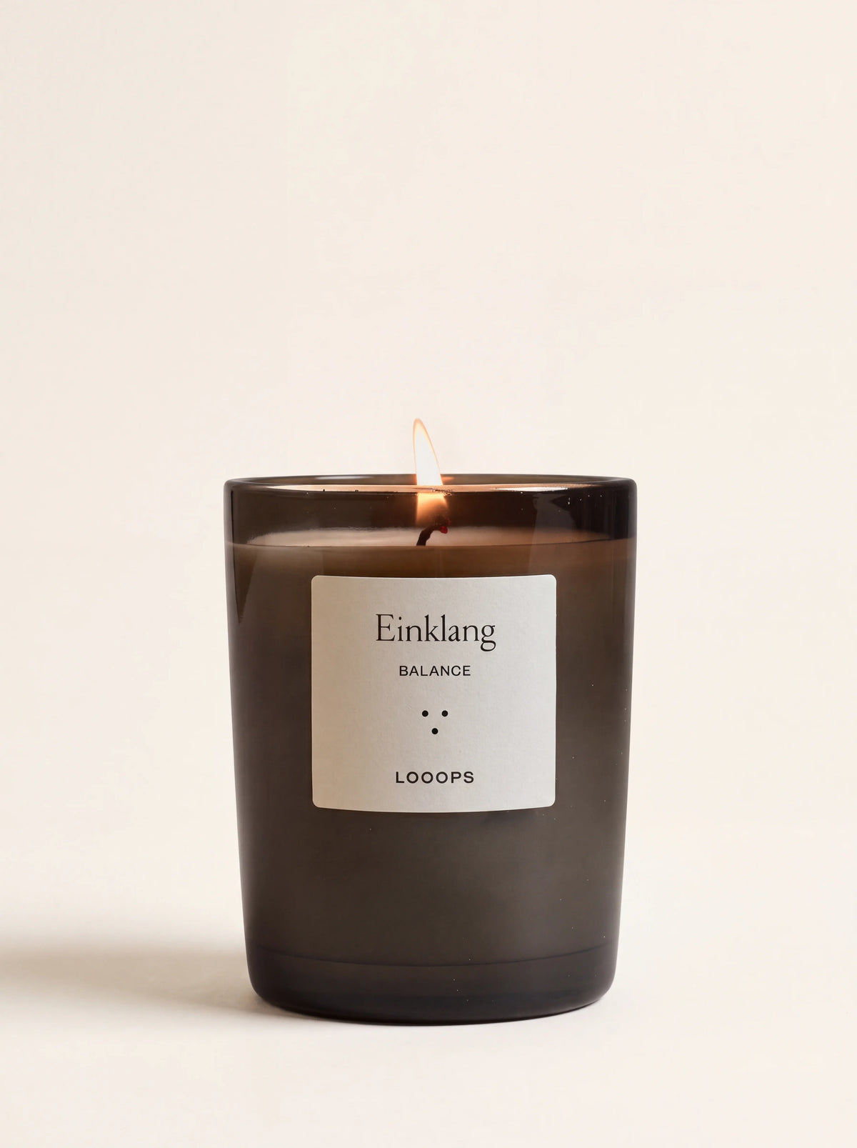 Lit scented candle in a dark glass jar, with a label reading Einklang BALANCE