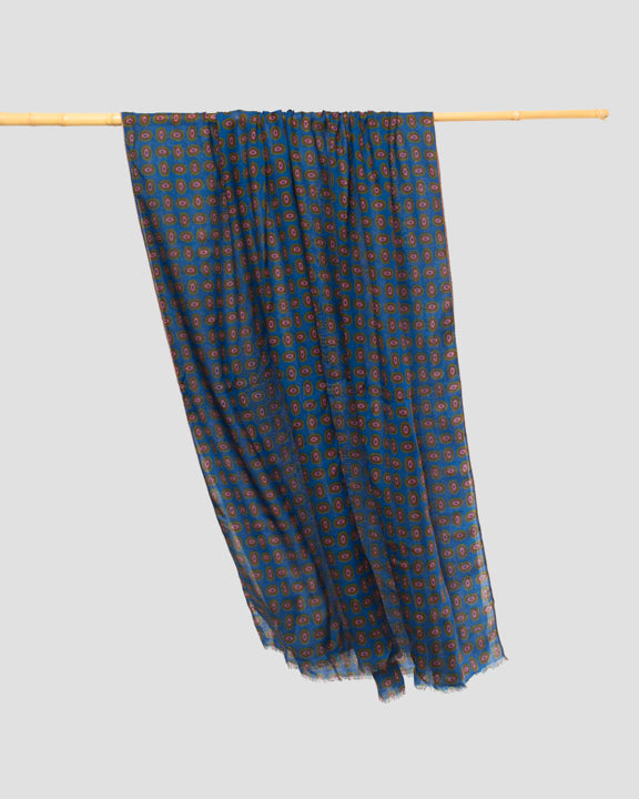 Blue wool scarf gathered and draped over a bamboo rail, displaying its lightweight semi-sheer fabric