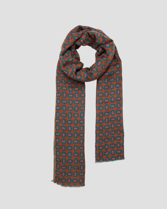 Brown wool scarf draped in a loop, patterned with concentric eye motifs in petrol, brown, and pink
