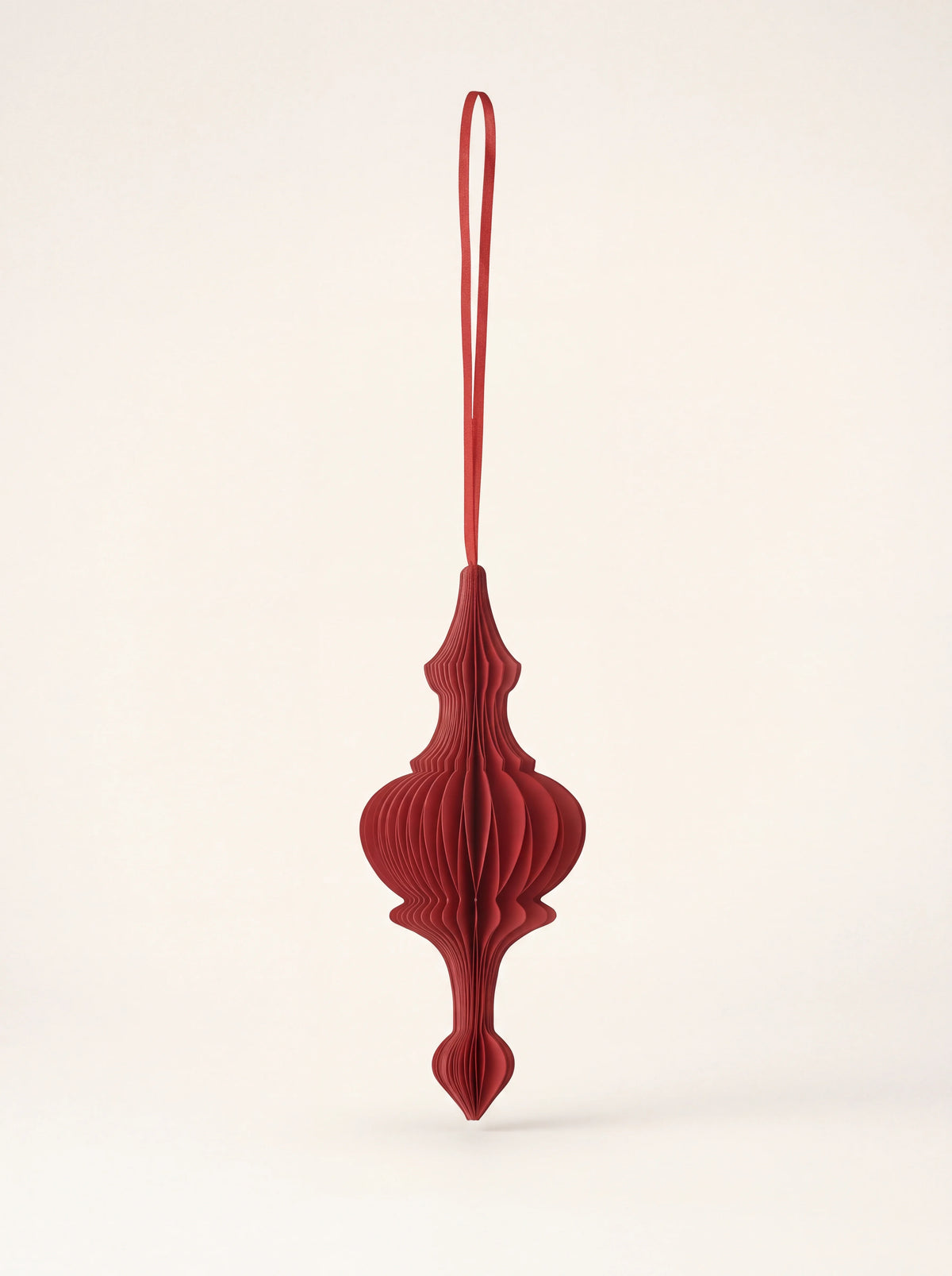 Ruby red honeycomb paper ornament in a flared finial shape with a hanging ribbon