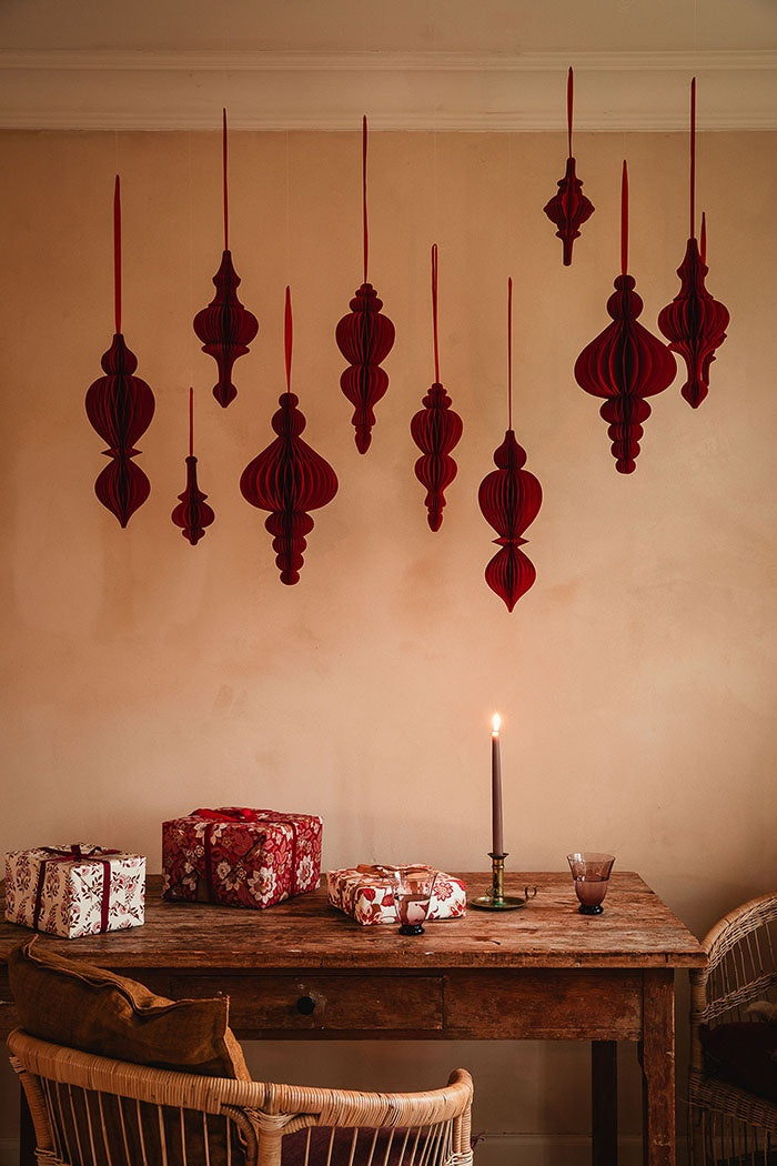 Ruby honeycomb ornaments hanging at varying heights above a wooden table arranged with wrapped gifts