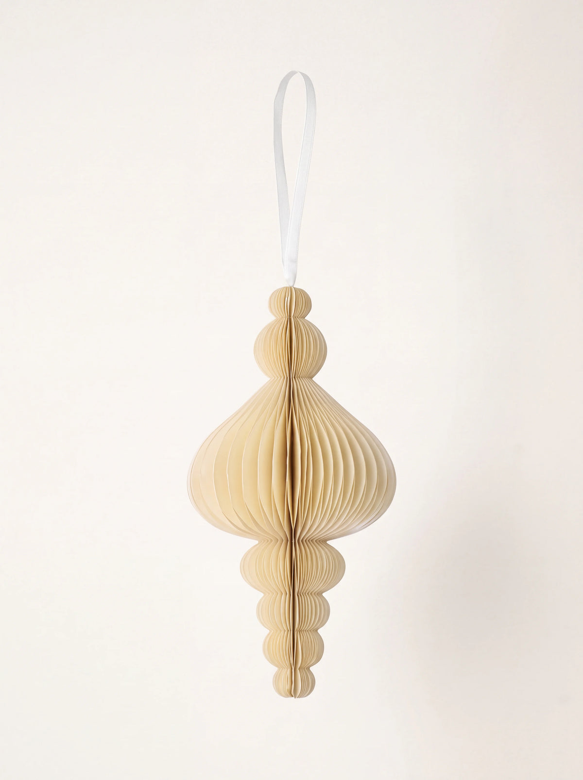 Tiered honeycomb paper ornament in light cream, hanging from a white ribbon loop