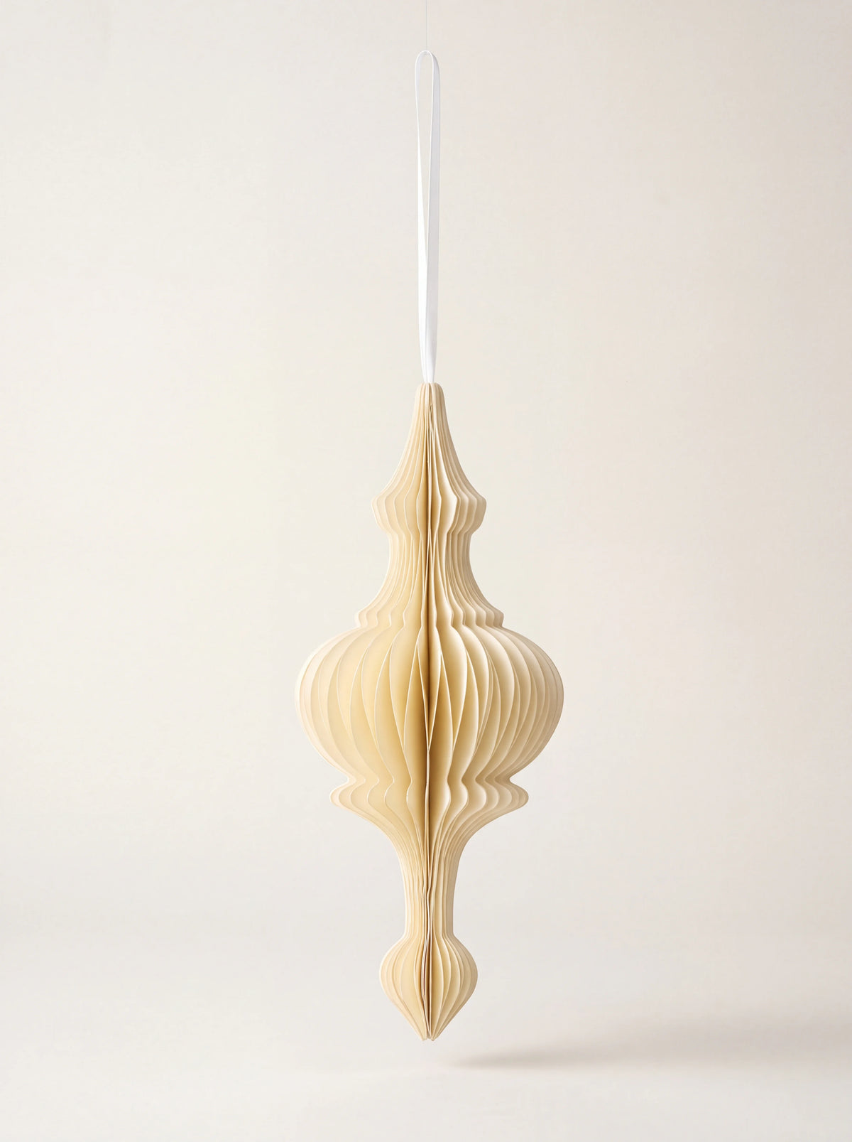 Cream paper honeycomb ornament with a tiered silhouette, suspended from a white ribbon