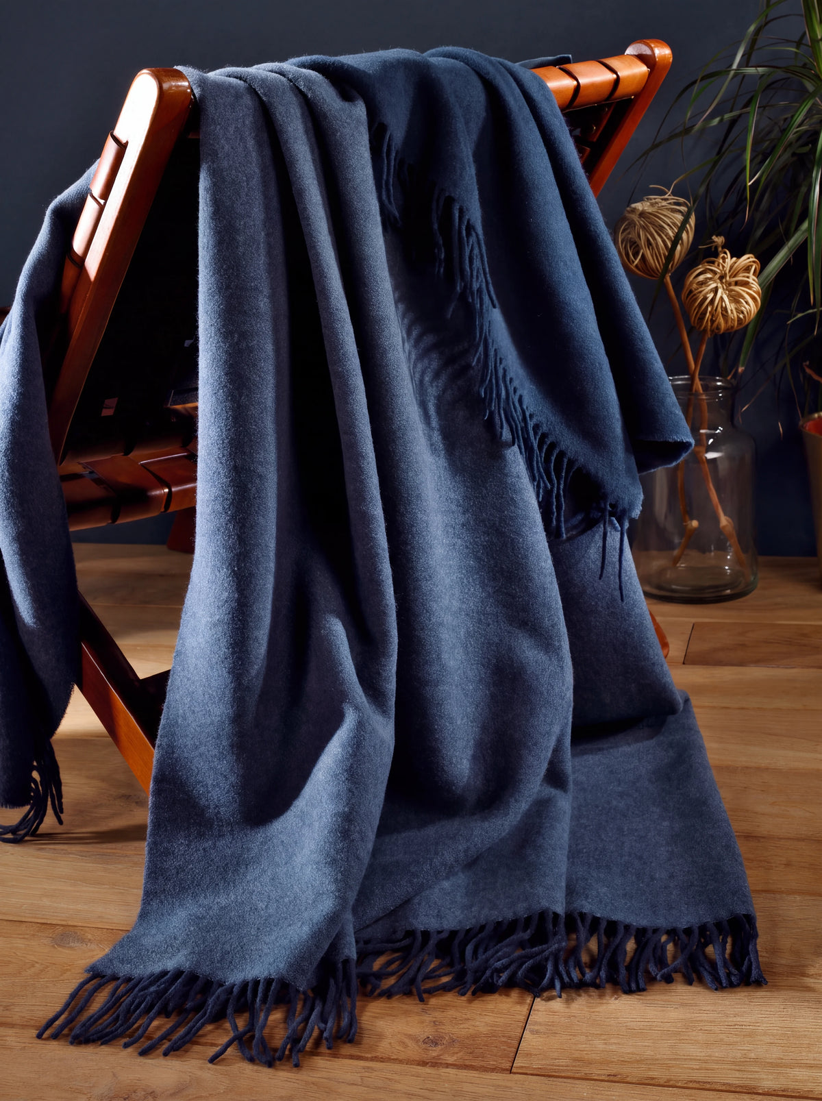 Wool and cashmere blanket draped over a wooden armchair, showing its soft texture and fringed hem