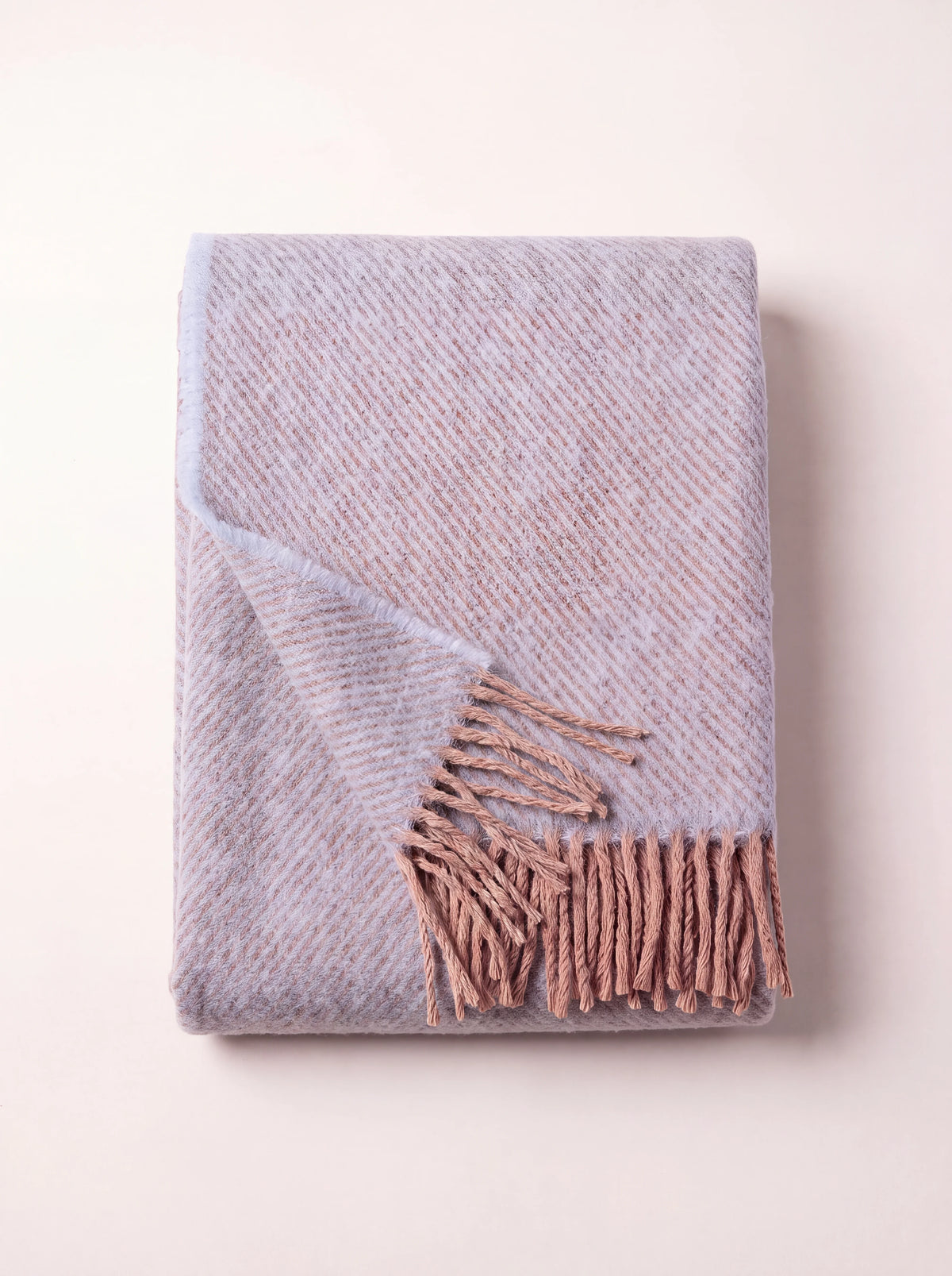 Folded powder and light blue wool blanket with diagonal twill weave and fringed edges