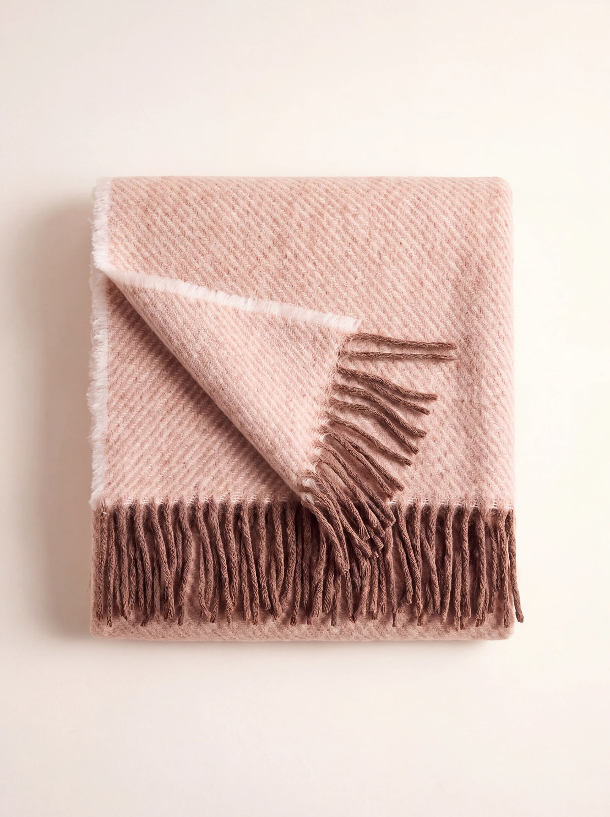 Wool blanket in a powder-pink twill weave, folded to display its brown fringed edges