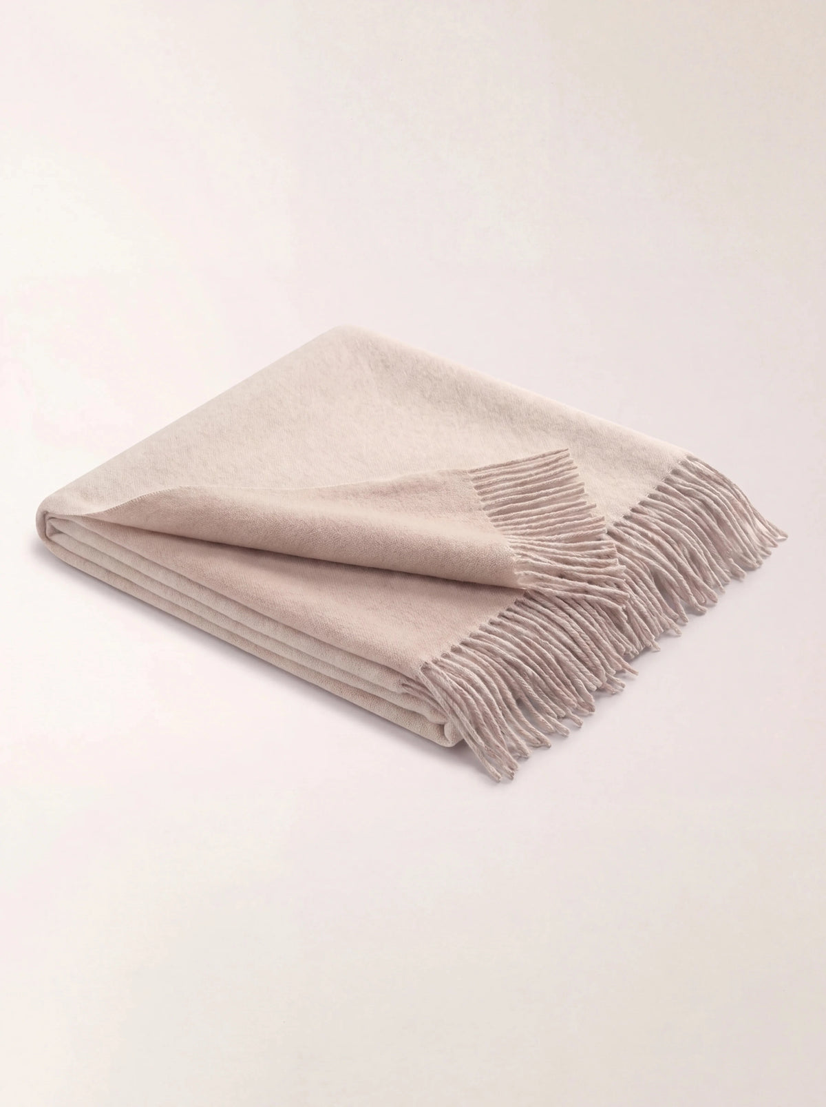 Beige wool throw folded flat, showing its fringed edges and contrasting natural beige sides