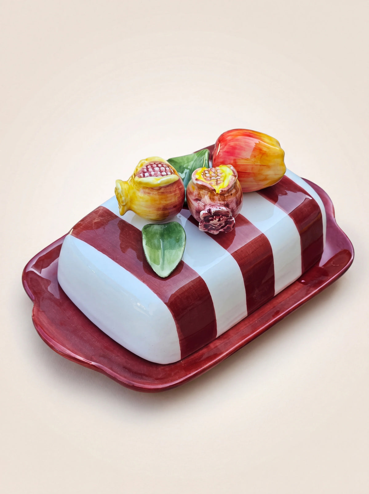 Ceramic butter dish with a red rectangular base and red-and-white striped lid topped with sculpted fruit