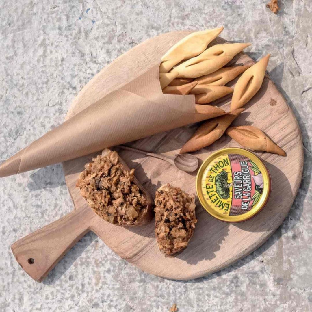 Flaked tuna spread on crusty bread slices, served with savoury biscuits on a wooden board