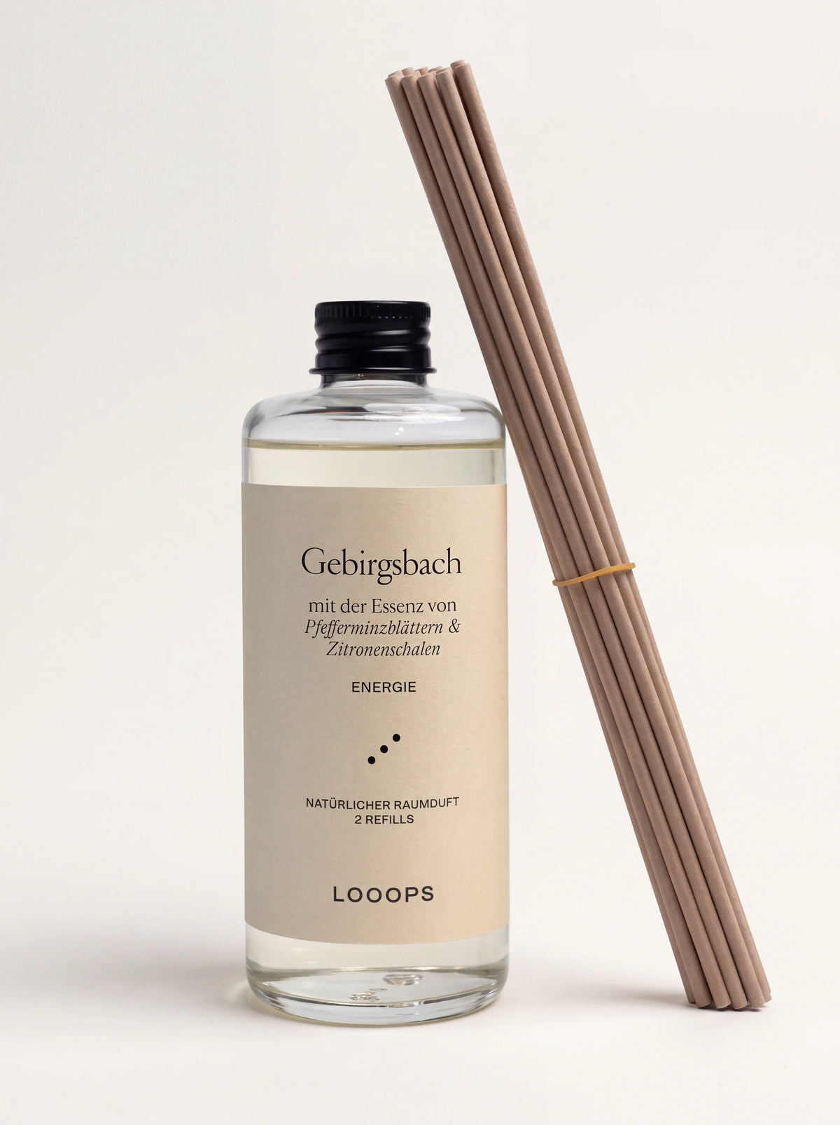 Reed diffuser refill in a clear glass bottle with black cap, standing beside a bundle of wooden diffuser reeds