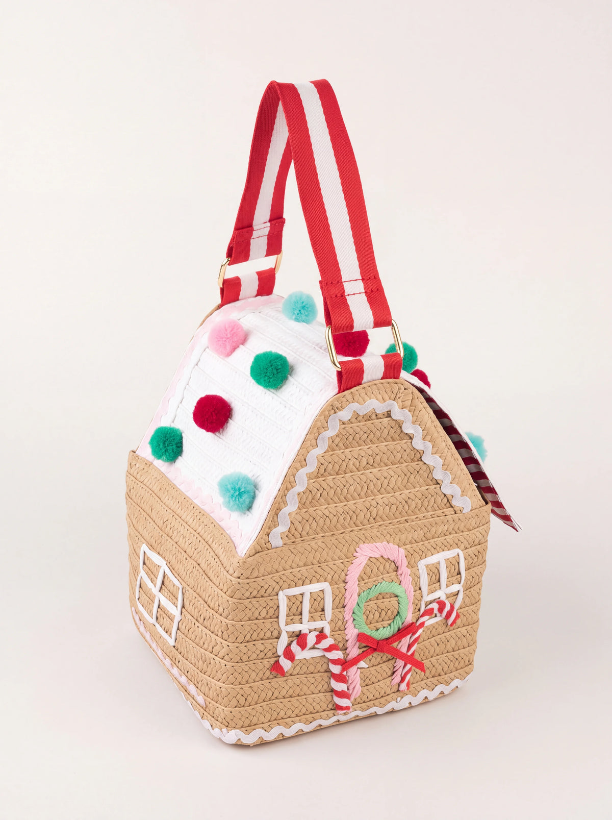 Gingerbread house-shaped woven paper bag with a pompom-trimmed roof and red-and-white striped handle