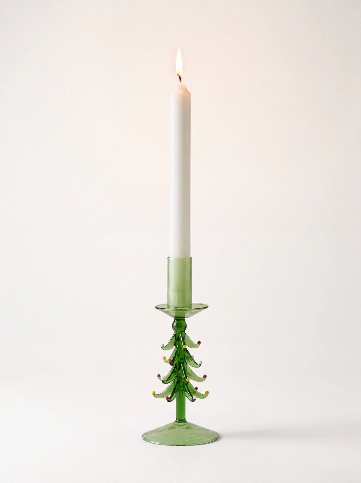 Green glass tree candle holder holding a lit white taper candle