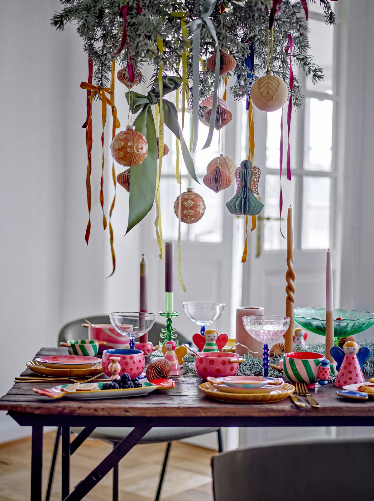 Green glass tree candle holder on a festive dining table set with colourful tableware and ornaments