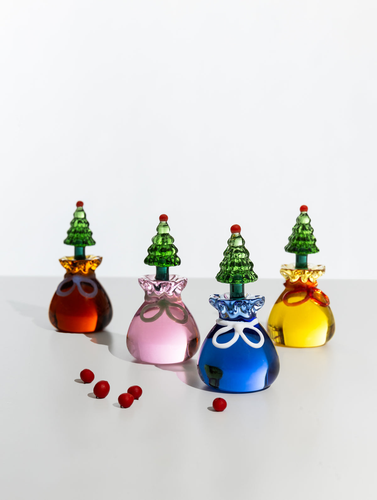 Four glass place markers in amber, pink, blue and yellow with green tree toppers, displayed together
