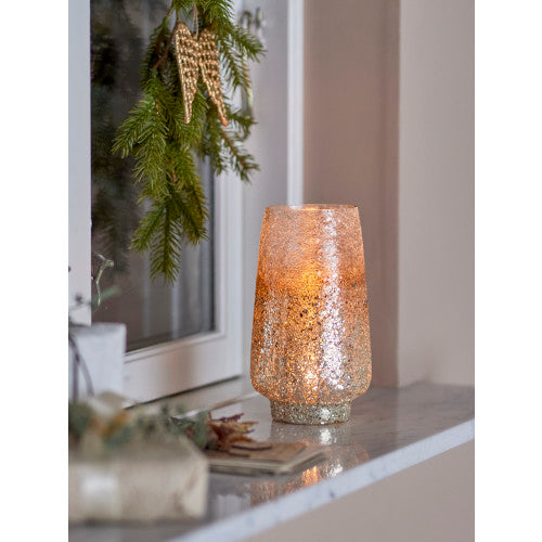 Glass tealight holder illuminated from within on a windowsill, showing a warm glow