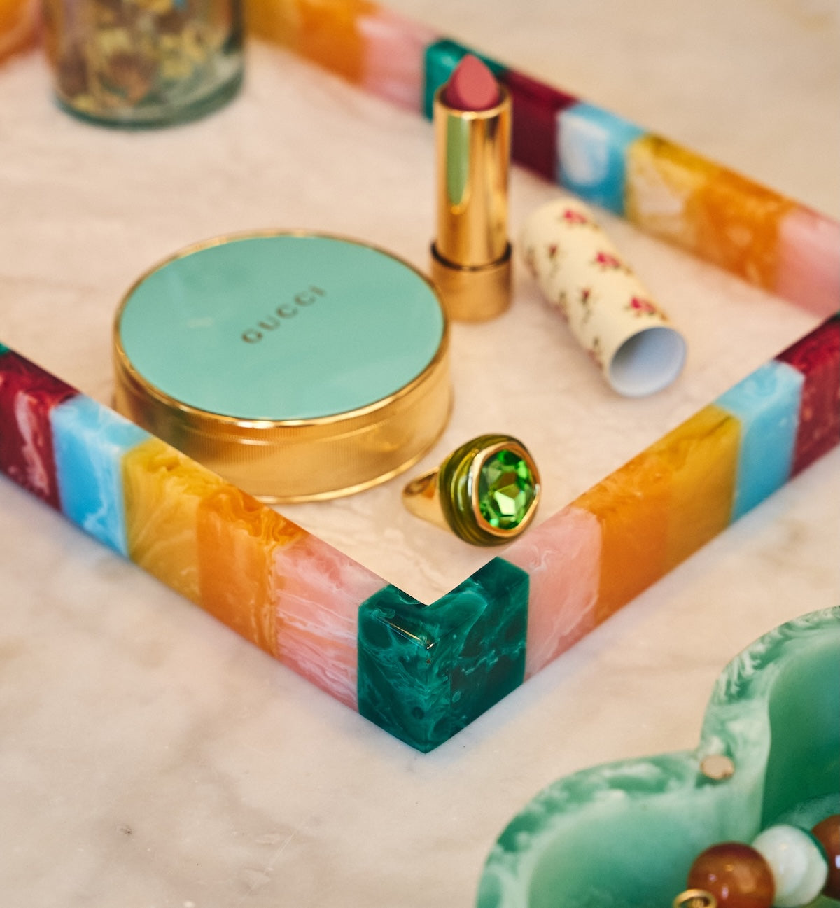 Close-up of the multicoloured resin tray holding a ring, lipstick and a compact marked GUCCI