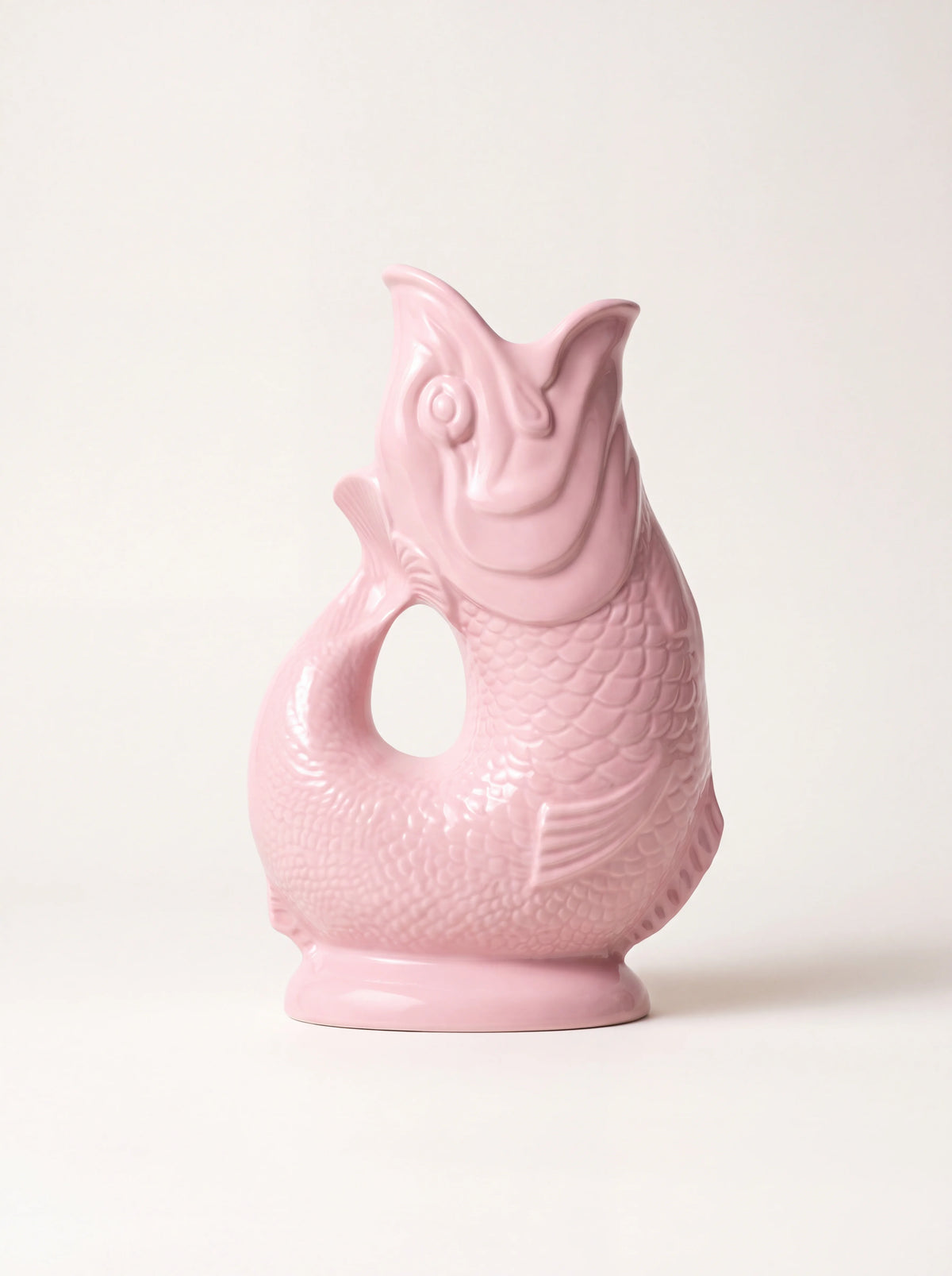 Baby pink ceramic gluggle jug shaped like a fish with an open mouth spout and curved tail handle