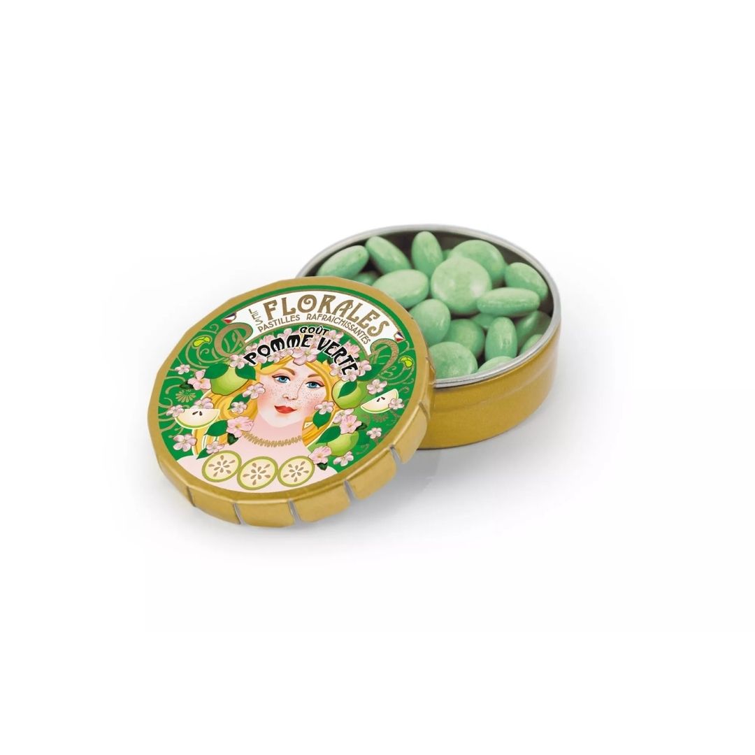 Open round gold-tone tin filled with light green pastilles, with the illustrated lid propped in front