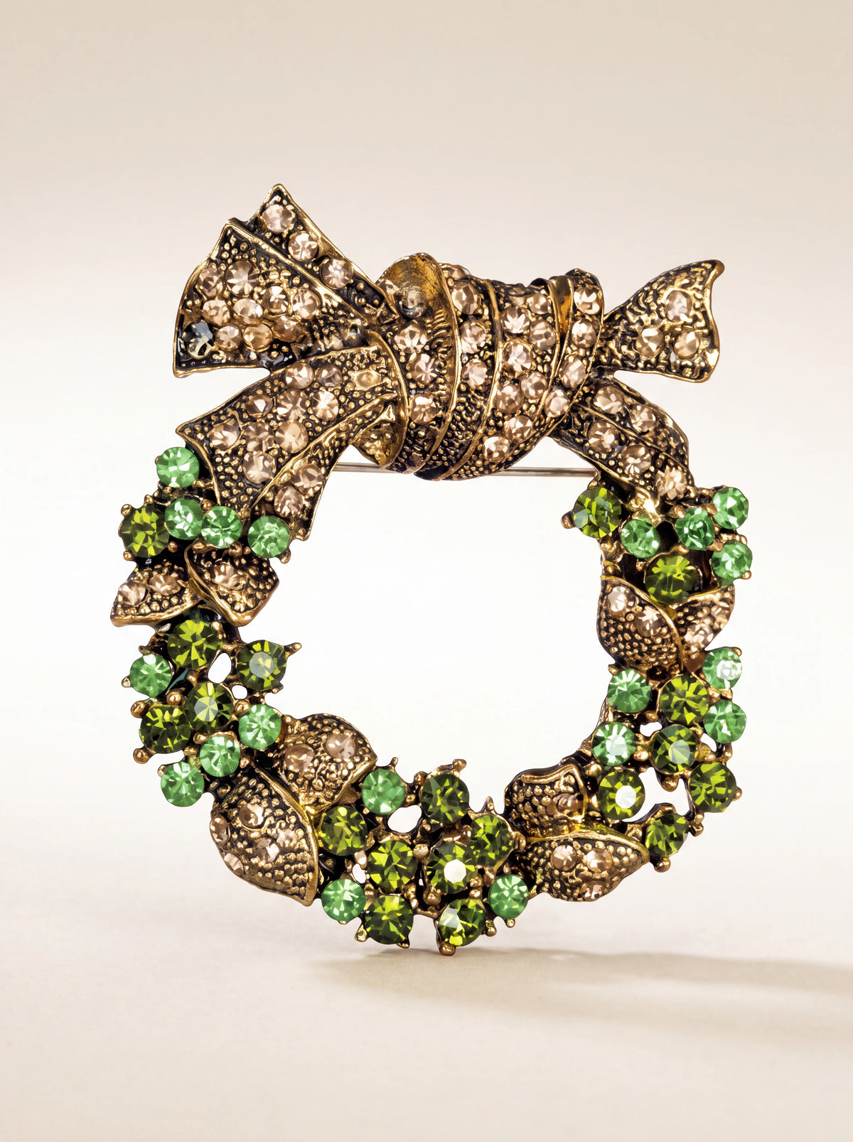Gold-toned wreath brooch with an ornate crystal bow and clusters of faceted green crystals