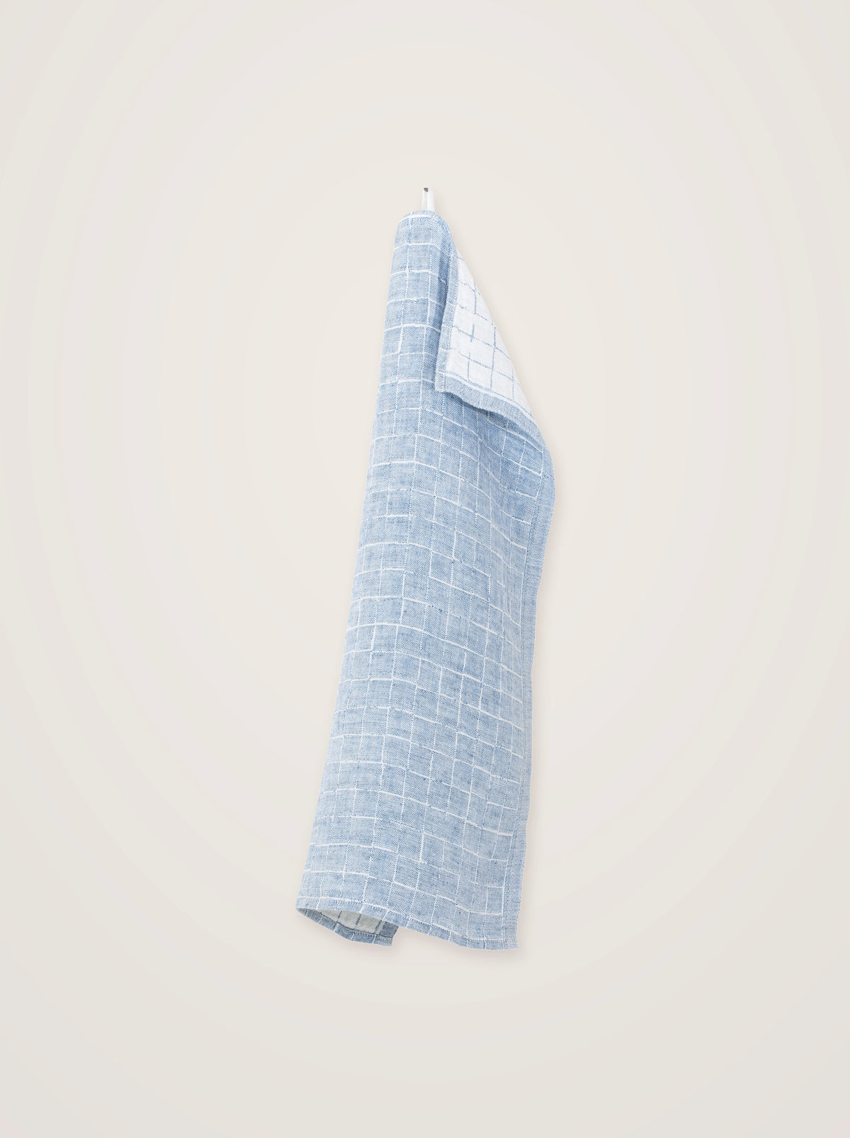 Blue washed linen towel hanging from a hook, showing its drape and grid pattern