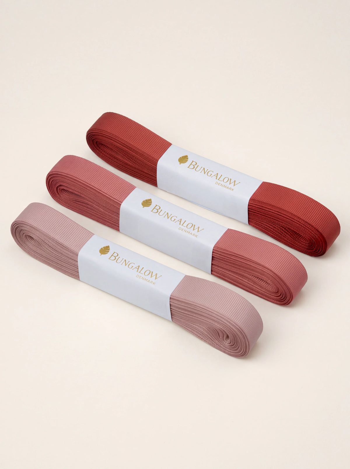 Set of three ribbed grosgrain ribbon bundles in graduated shades of cinnabar red, rose and dusty pink