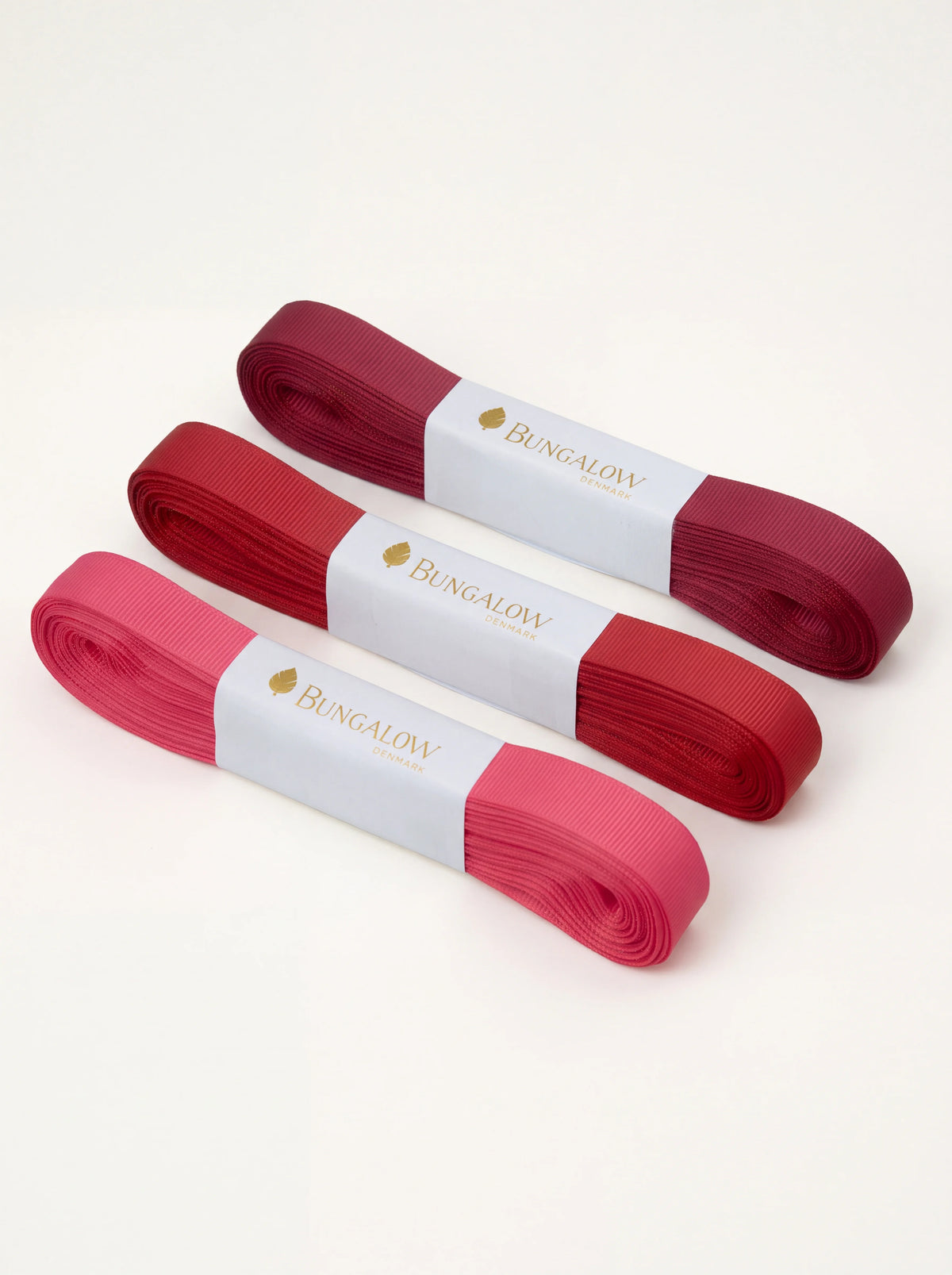 Grosgrain ribbon set of three in tonal ruby shades, rolled and held with paper bands