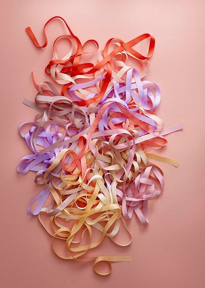 Grosgrain ribbons unrolled and looped in a loose tangle of pastel and ruby shades