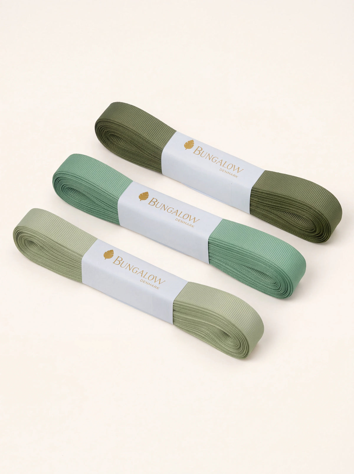 Three bundles of ribbed grosgrain ribbon in light, medium and dark sage green with paper sleeves