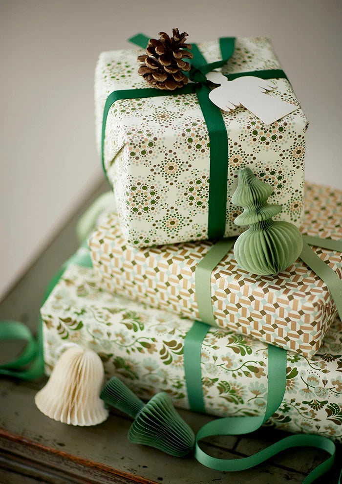 Sage green ribbon tied around a stack of patterned gift boxes decorated with paper ornaments