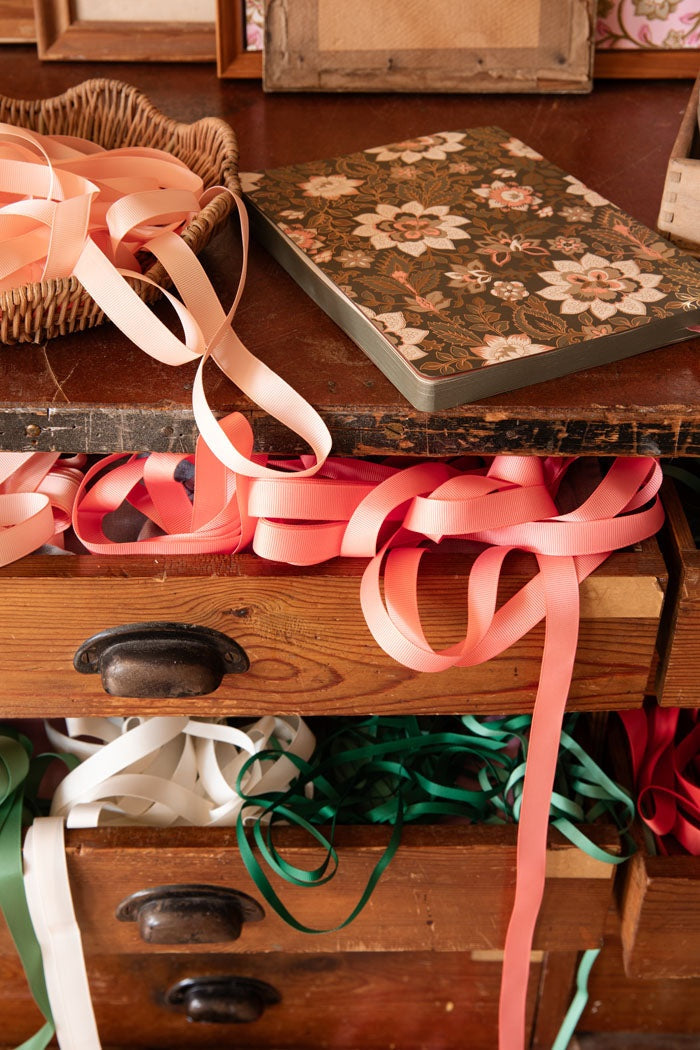Unwound grosgrain ribbons trailing from an open wooden drawer and a woven basket