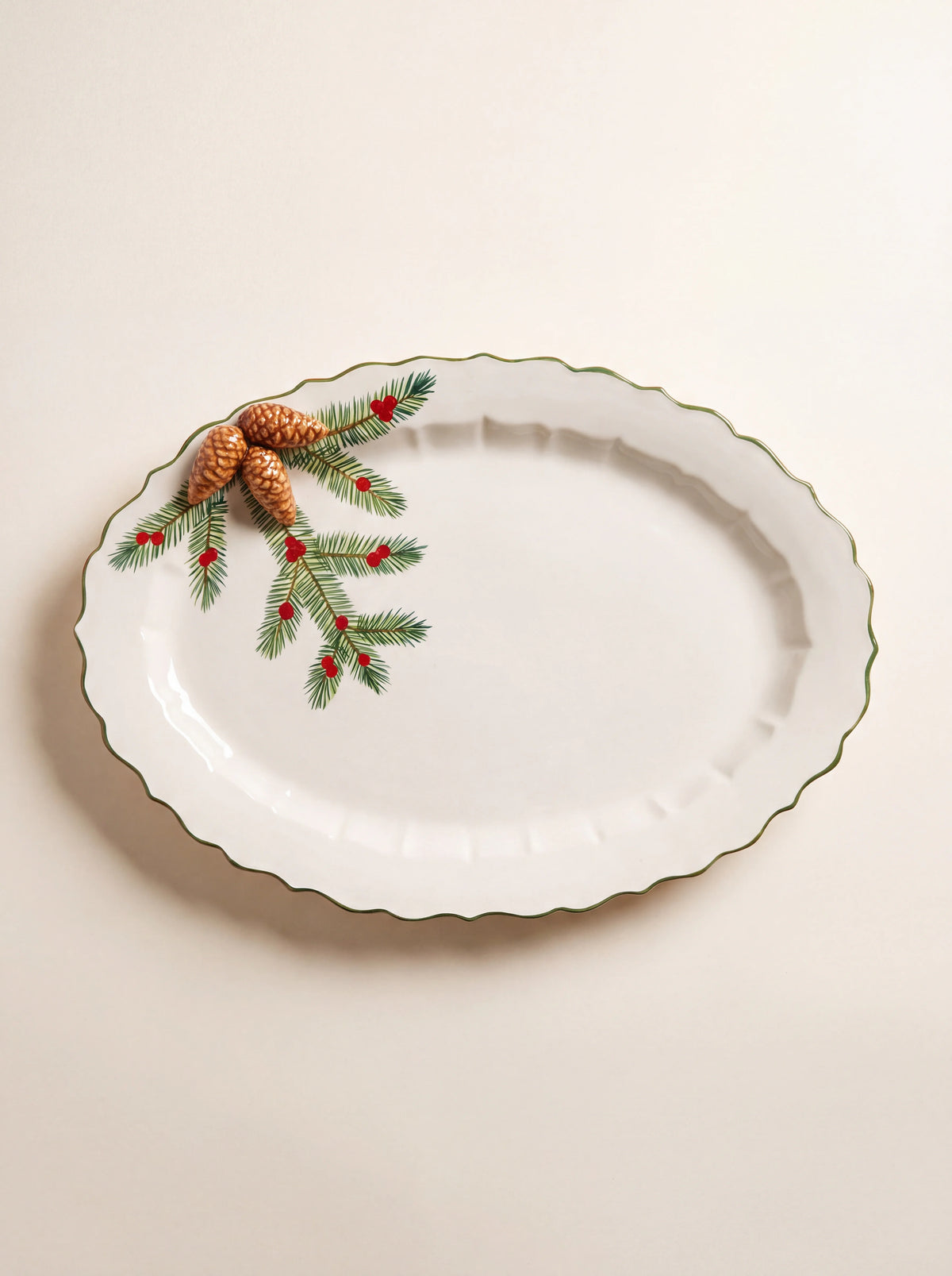 Oval ceramic tray with a scalloped green rim, pine branch motif, red berries and three raised pine cones