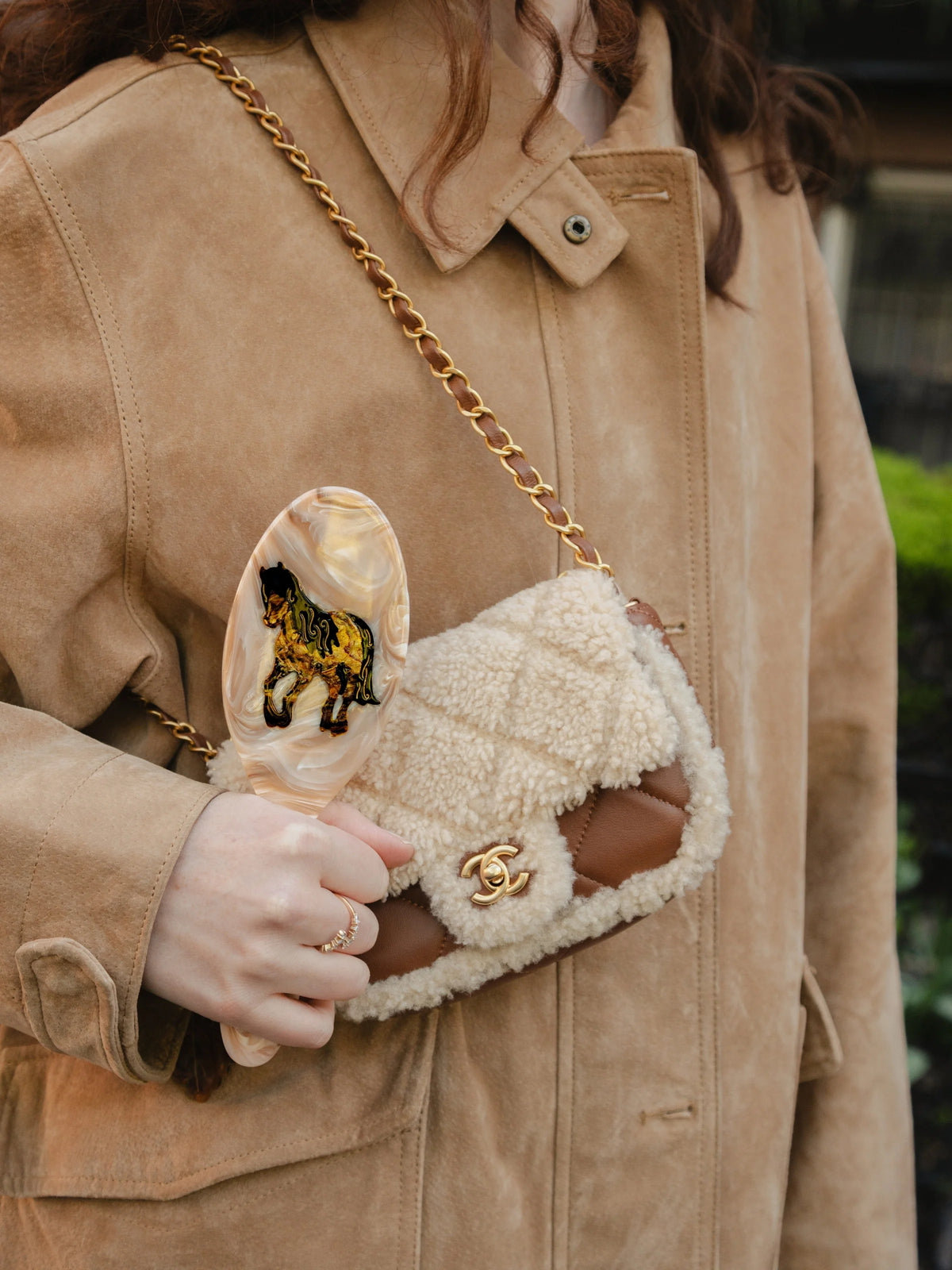 Acetate hairbrush held in one hand, showing its scale against a coat and small handbag
