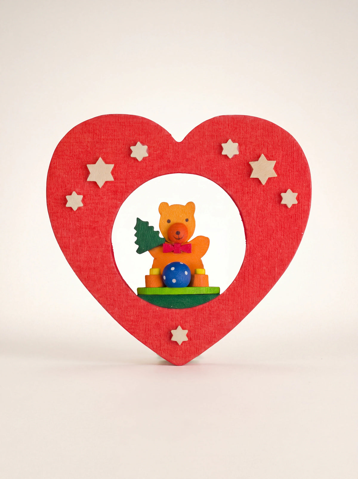 Red maple wood heart ornament with small wooden stars and a painted teddy bear sitting inside the cut-out