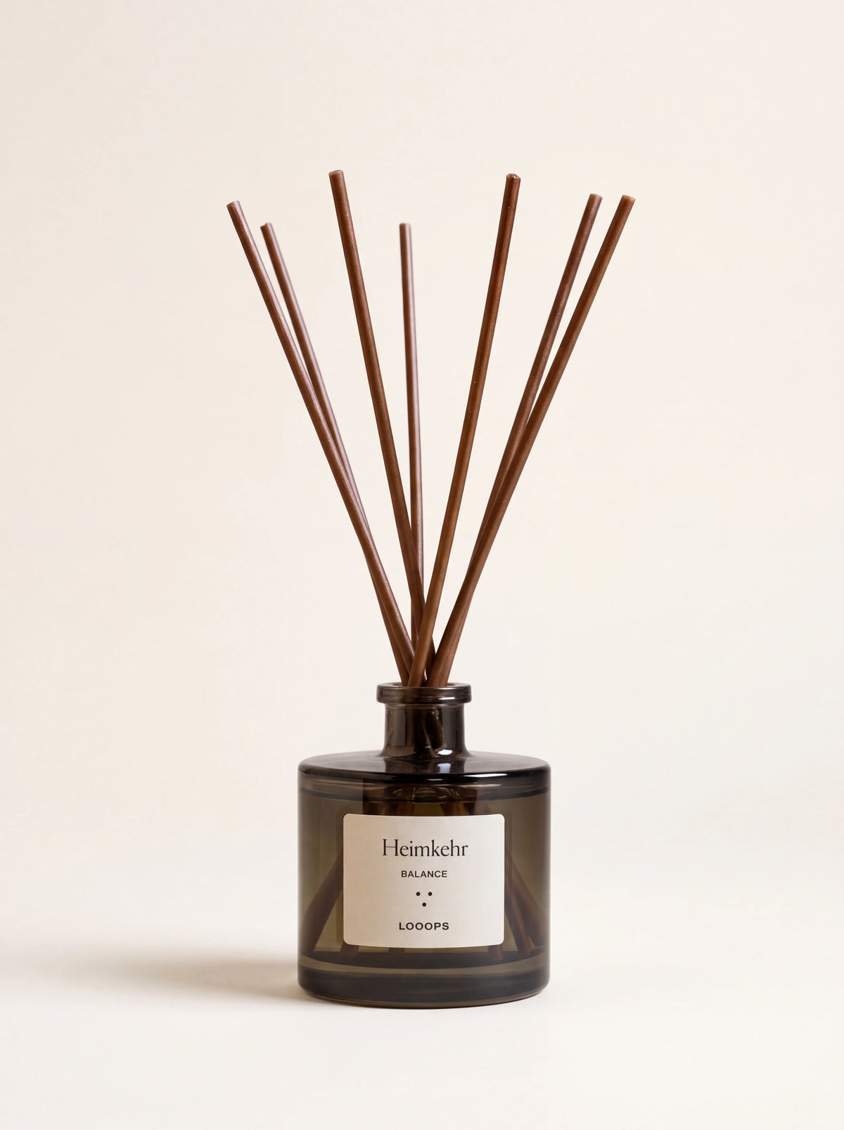 Glass reed diffuser in a smoky glass bottle with brown paper reeds, labelled Heimkehr BALANCE LOOOPS