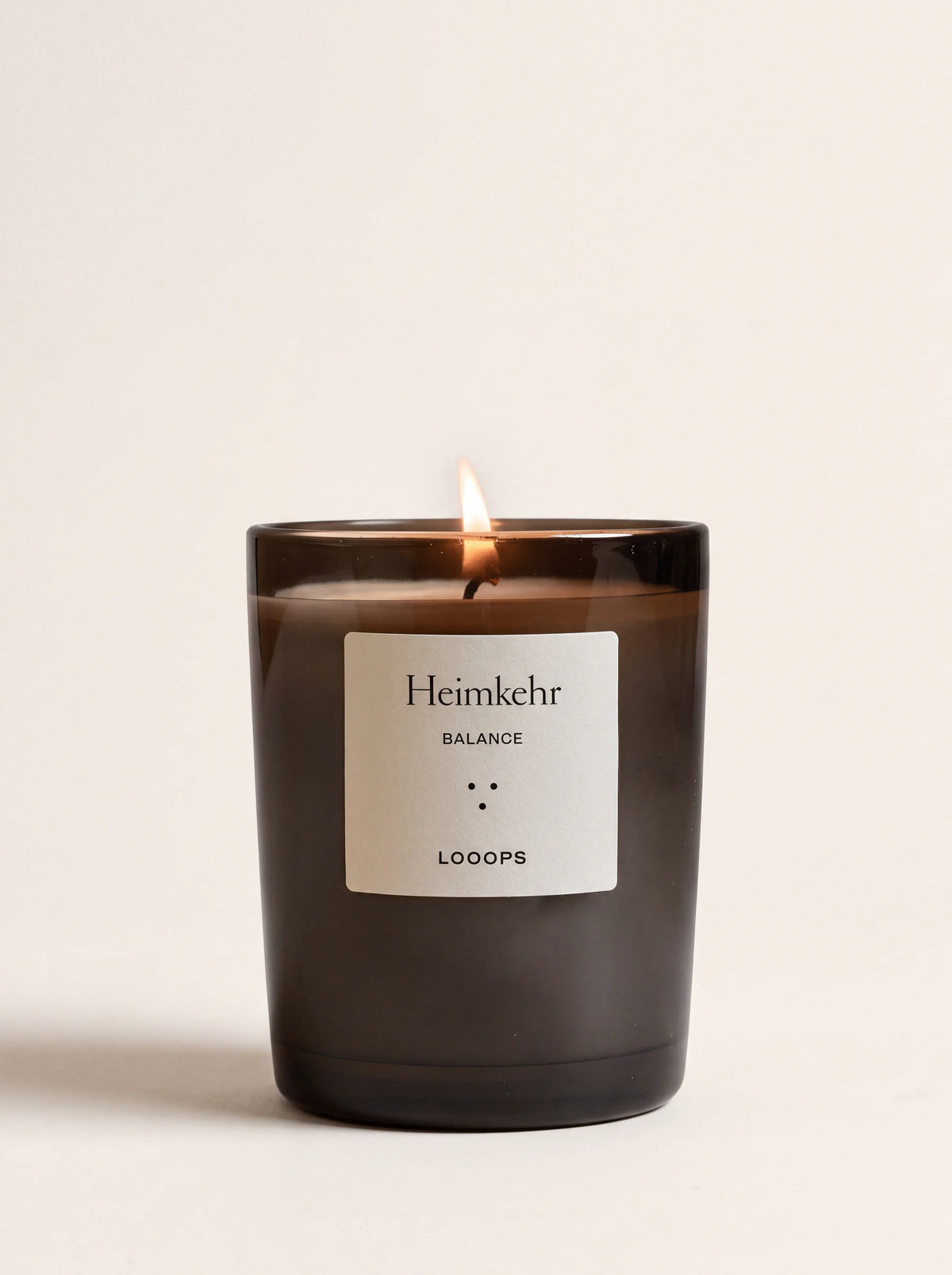 Lit scented candle in a dark smoked-glass jar with a label reading Heimkehr BALANCE