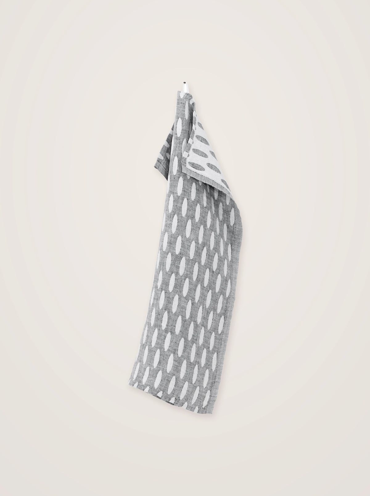 Grey and white washed linen towel hanging vertically, showing the drape and reversible oval pattern