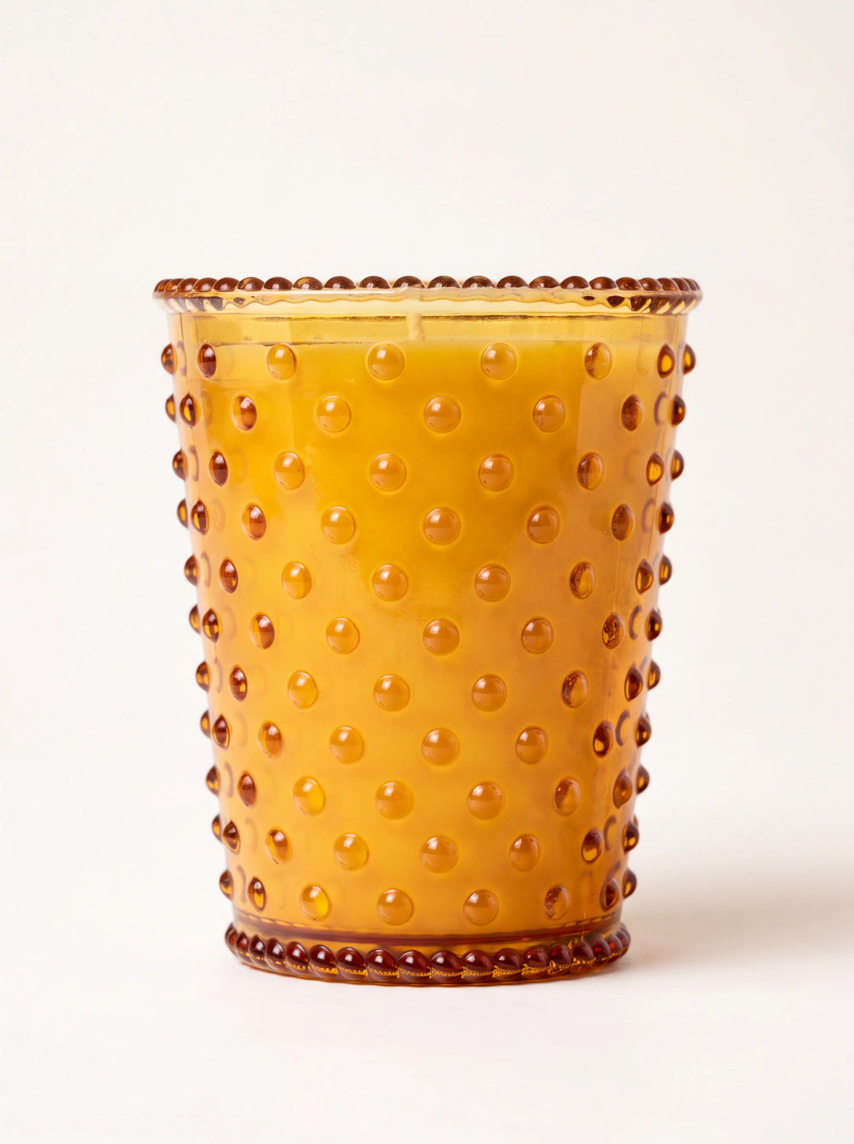 Scented candle in an amber hobnail glass vessel with raised dots and a beaded rim