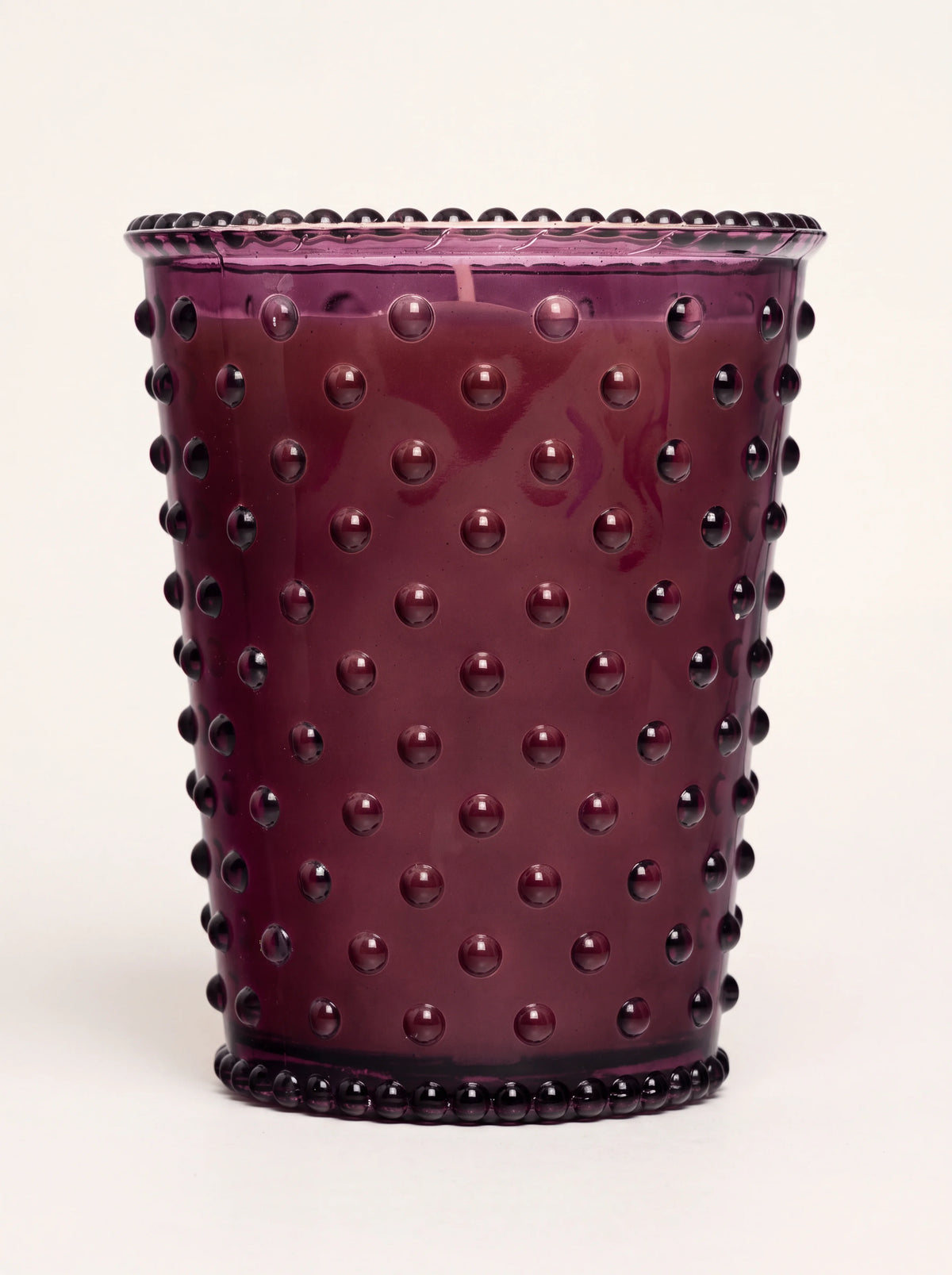 Scented candle in a deep purple hobnail glass with studded texture and a beaded rim