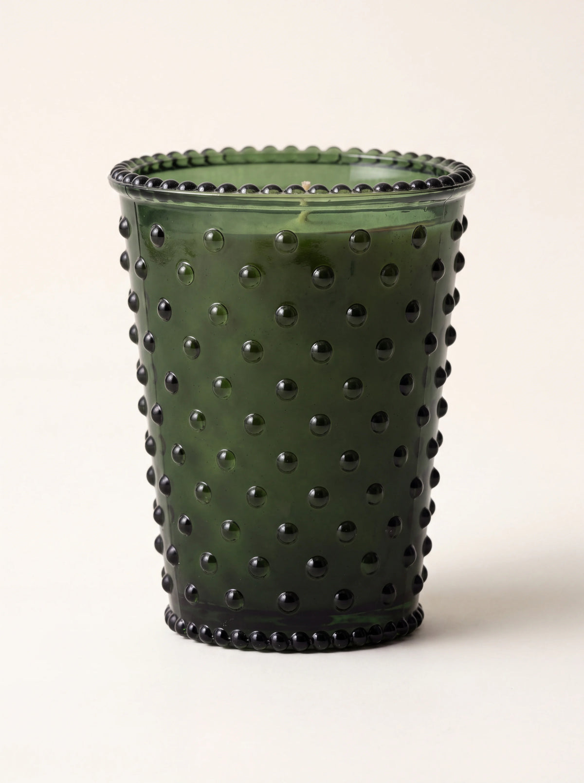 Scented candle in dark green hobnail glass with raised studs and a beaded rim
