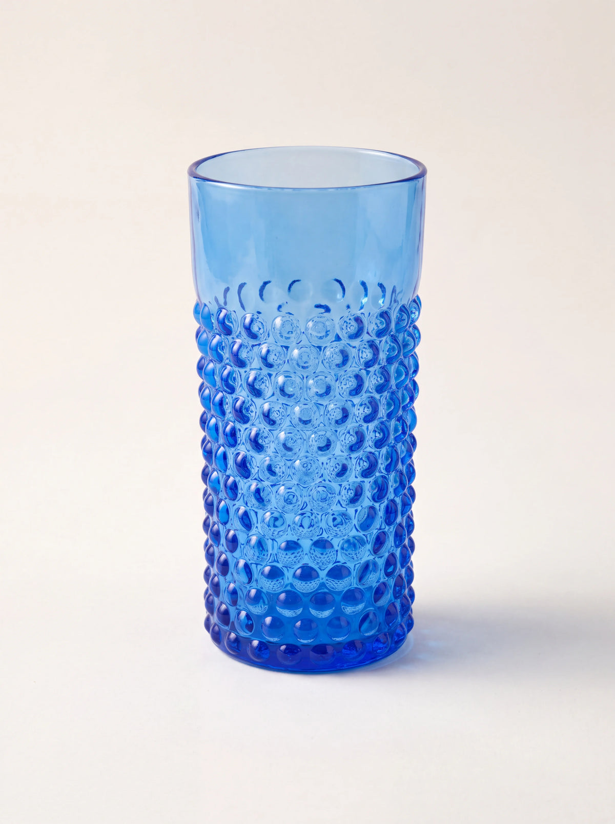 Cylindrical blue glass tumbler with a raised hobnail texture and a smooth upper rim