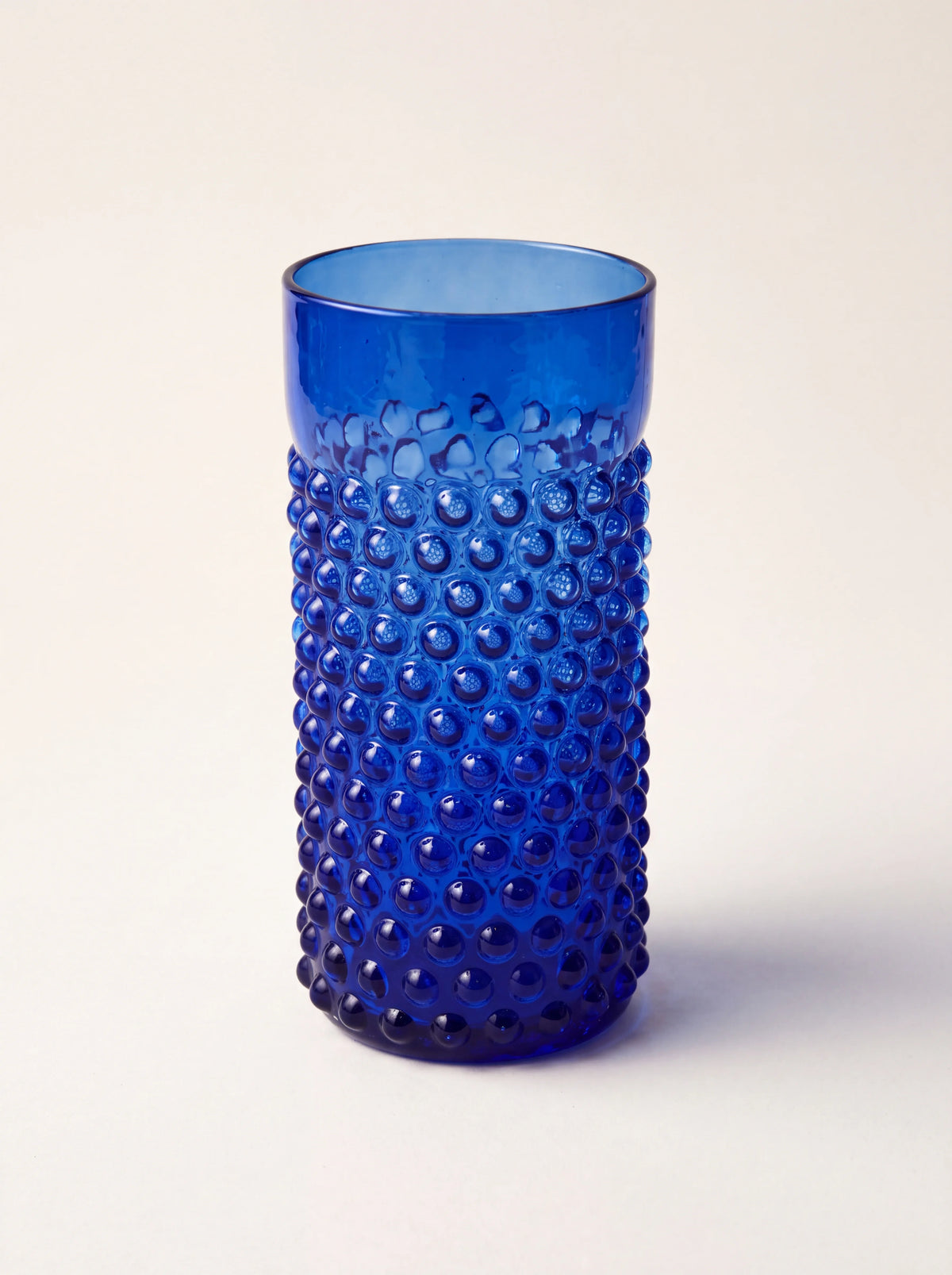 Dark blue hobnail glass tumbler with a cylindrical shape and smooth upper rim
