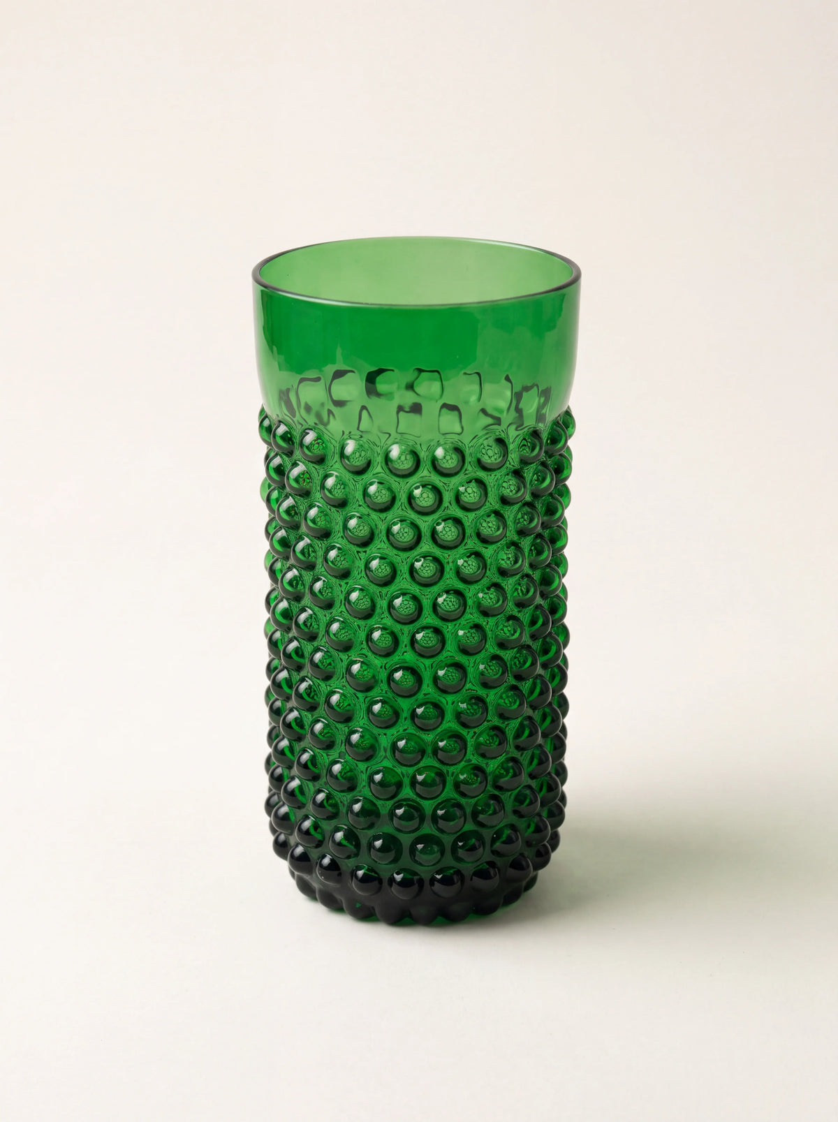 Cylindrical dark green glass tumbler with a raised hobnail texture and a smooth upper rim