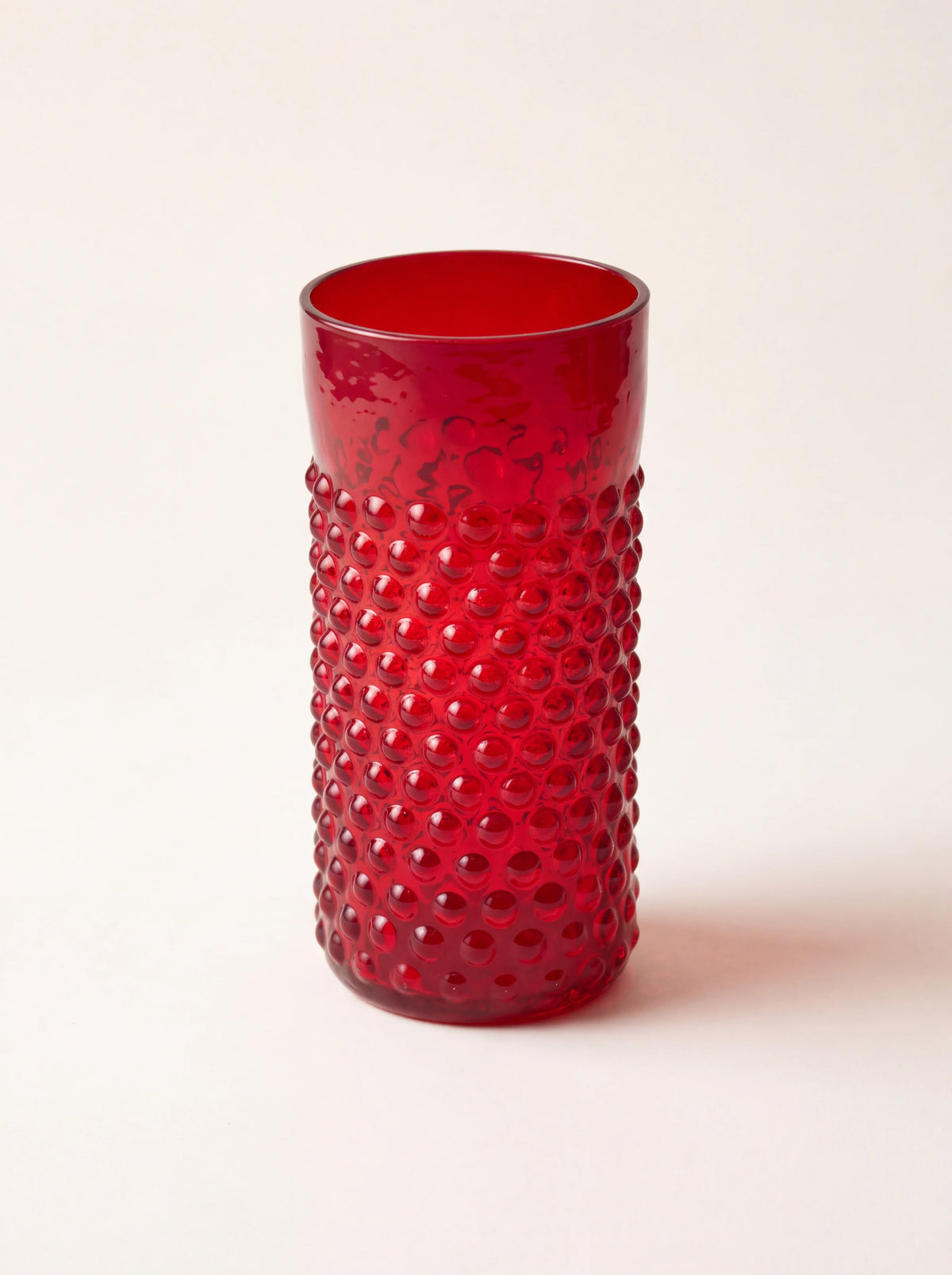 Tall cylindrical garnet red glass tumbler with a raised hobnail texture and smooth upper rim