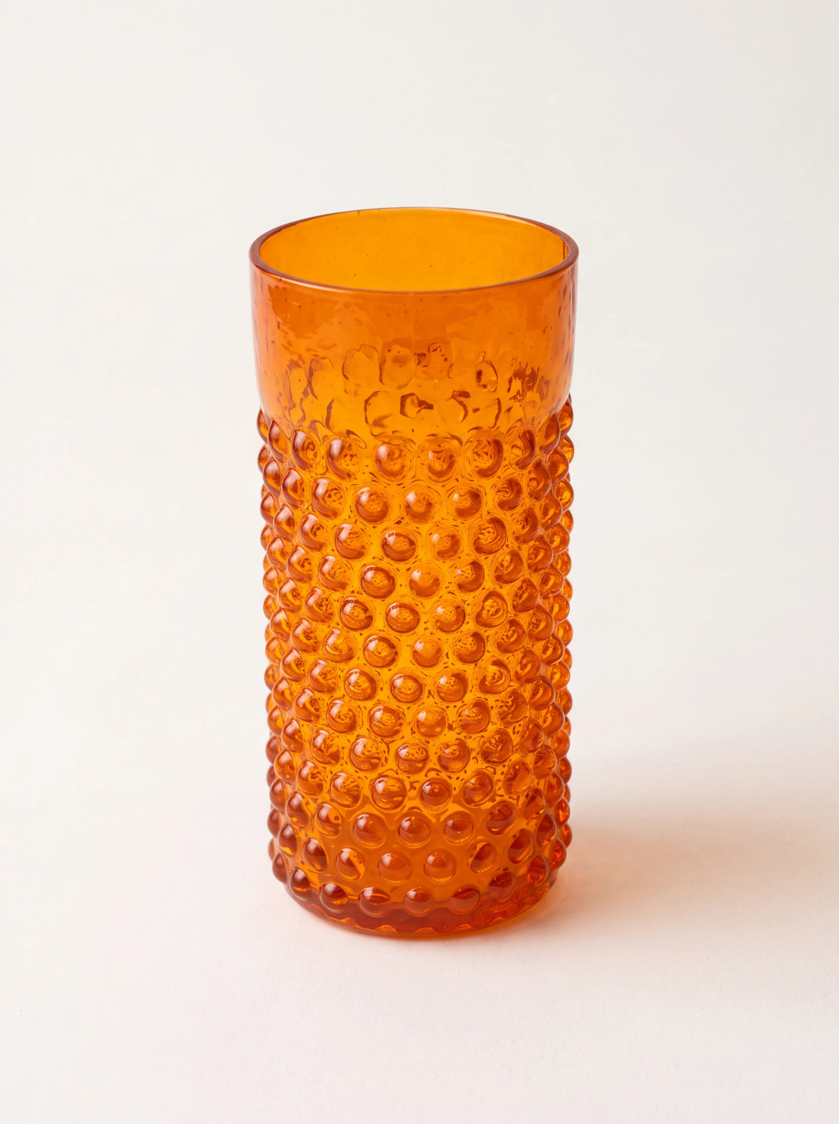 Cylindrical orange glass tumbler with raised hobnail texture and a smooth rim